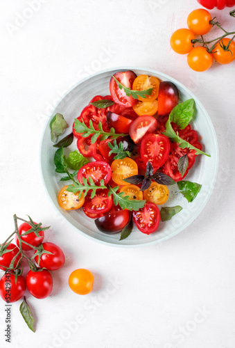 Salad with red, black and yellow cherry tomatoes, arugula and basil dressed with black salt and olive oil served on wheat straw plate. Top view