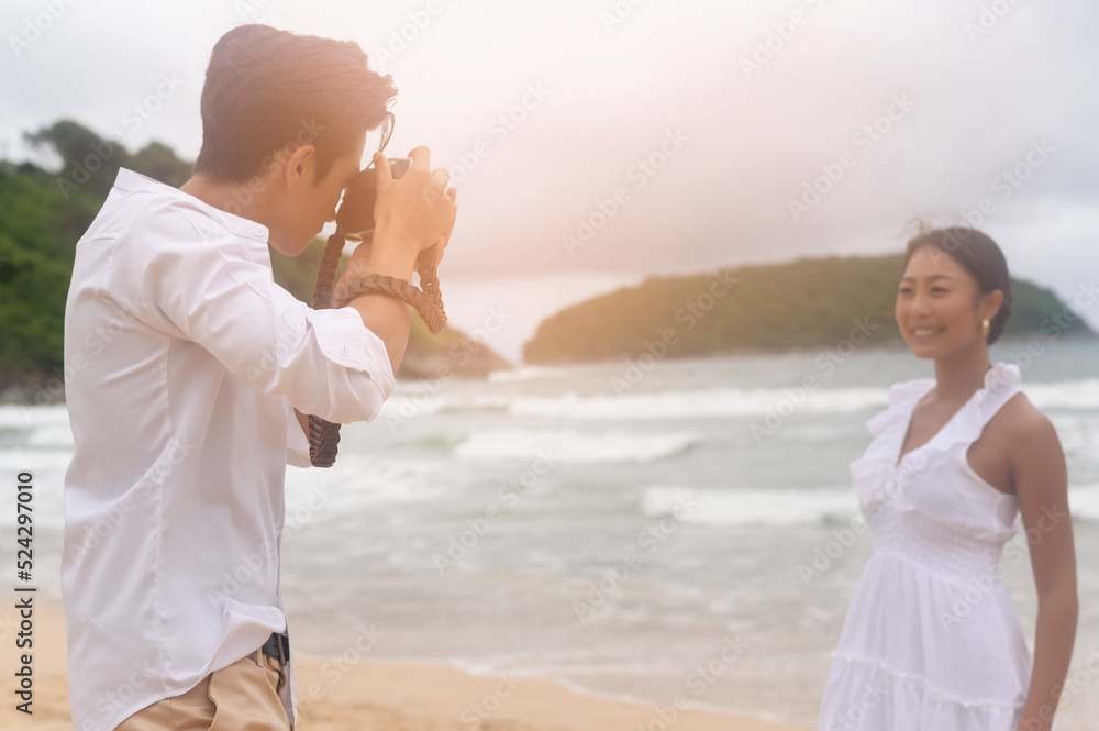 Happy young couple wearing white dress enjoy taking photo on the beach on holidays, travel, romantic, wedding concept