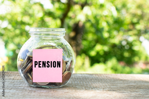 A glass jar with coins and the inscription PENSION on a wooden table. Budget for investing.