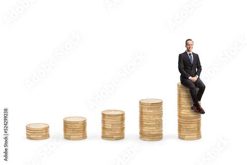Professional man in suit and tie sitting on a rising piles of coins and looking at camera