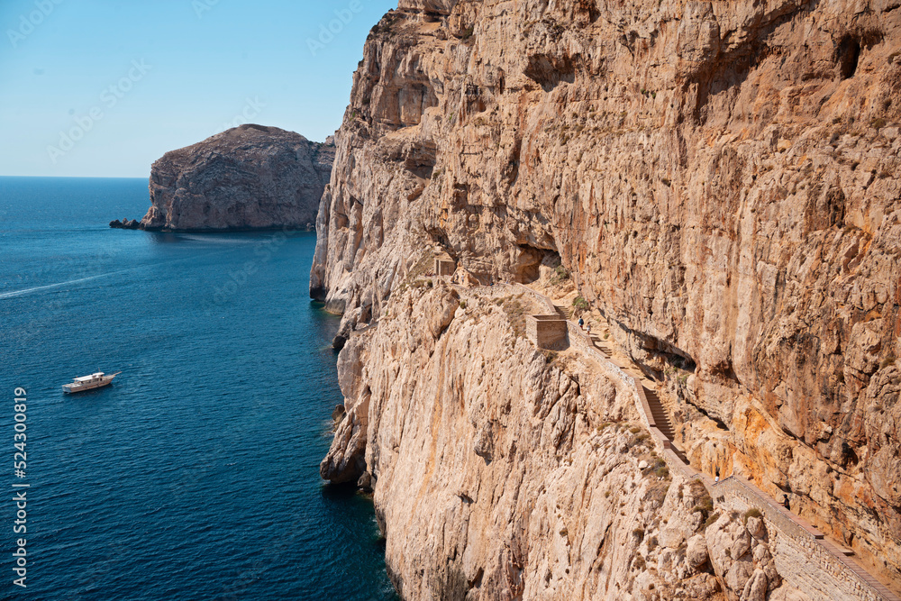 Obraz premium Stairway in limestone rock to stalactite Neptune cave. Boat leaving Grotte di Nettuno in Sardinia, Italy