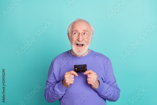 Photo of excited positive granddad arms hold plastic debit card look empty space isolated on turquoise color background © deagreez