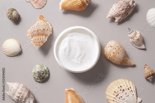 Container with bodycare and skincare cream on a grey background with seashell, summer skincare, soothing cream for face and body
