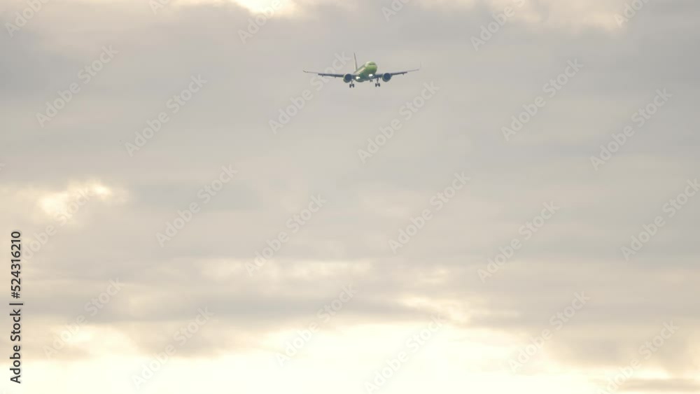 Long shot of jet passenger airplane approaching to land in a cloudy sky. Slow motion, airliner is flying. Tourism and travel concept Long shot of jet passenger airplane approaching to land in a cloudy sky. Slow motion, airliner is flying. Tourism and travel concept