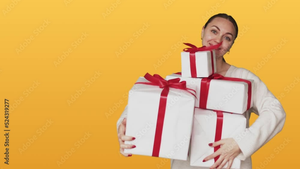 Happy white lady holding big stack of holiday gifts on yellow studio background. Smiling brunette woman with pile of festive presents, white boxes with red ribbons Happy white lady holding big stack of holiday gifts on yellow studio background. Smiling brunette woman with pile of festive presents, white boxes with red ribbons