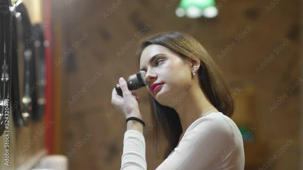 Side view of a woman using powder with a makeup brush in front of a mirror, a happy woman using cosmetics for beauty Side view of a woman using powder with a makeup brush in front of a mirror, a happy woman using cosmetics for beauty