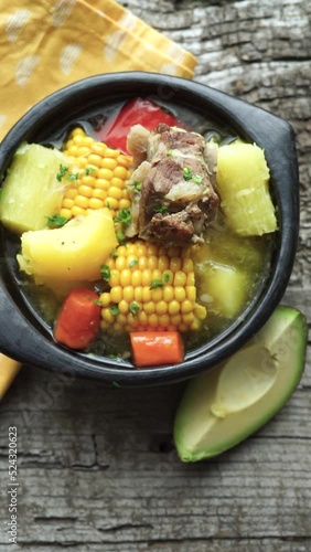 Typical Colombian Sancocho in a black ceramic bowl on a rustic wooden base. Vertical video.
