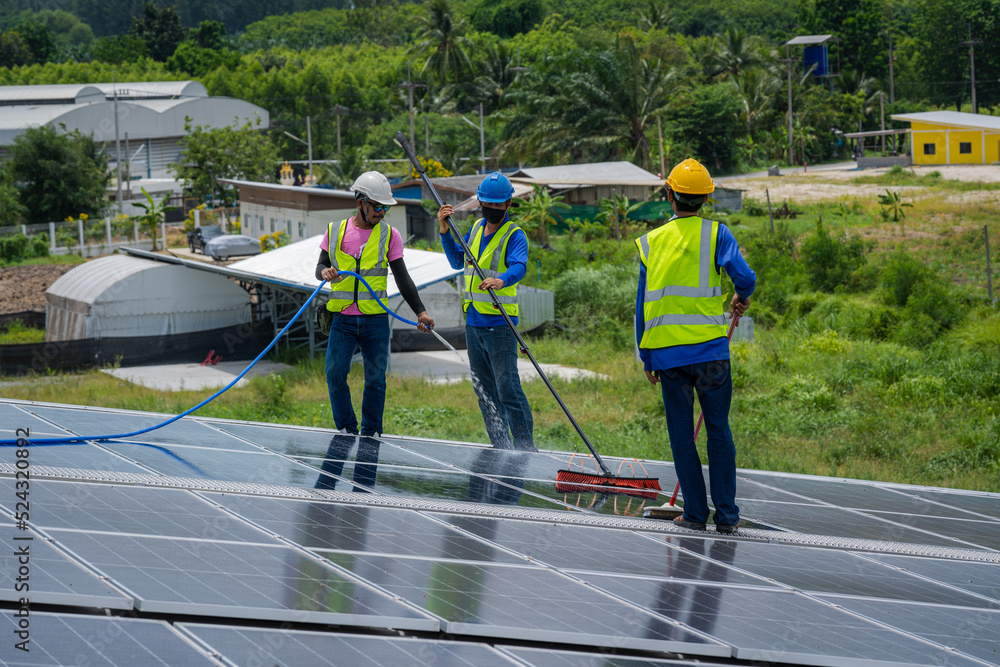 Professional worker cleaning solar panels with brush and water on roof structure of building factory.