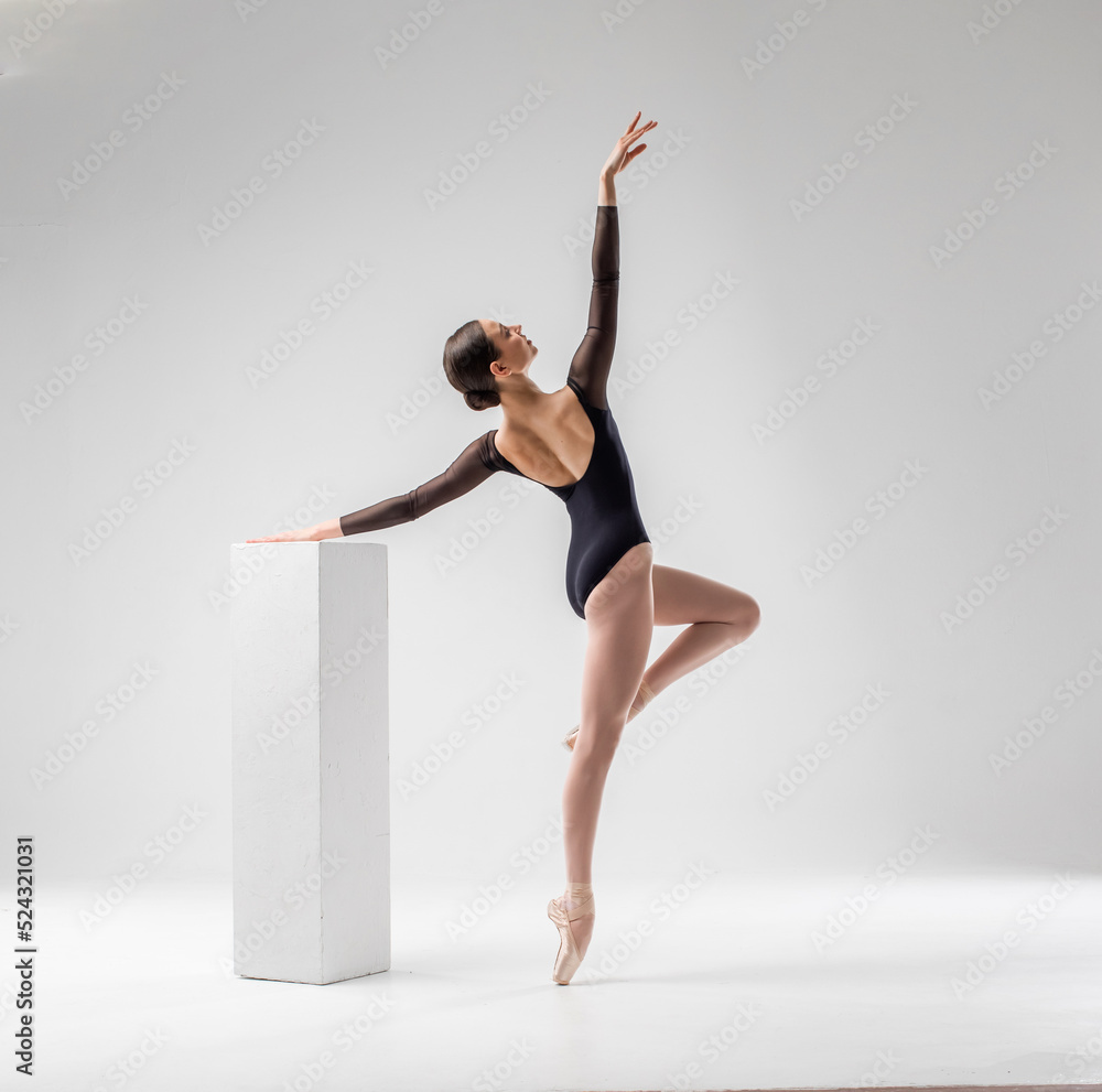 Ballerina in dark ballet leotard dancing on ballet pointe shoes in white studio  - obrazy, fototapety, plakaty 