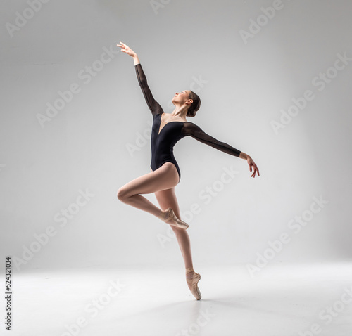 Ballerina in dark ballet leotard dancing on ballet pointe shoes in white studio 