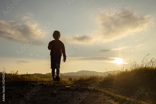 Sweet toddler child, boy, sitting on a haystack in field on sunrise