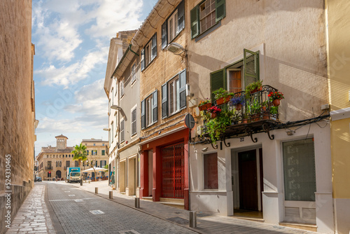 Picturesque street with flowers on the balcony of a home and shops in the hilltop city of Mahon or Mao, Spain, on the Mediterranean island of Menorca.