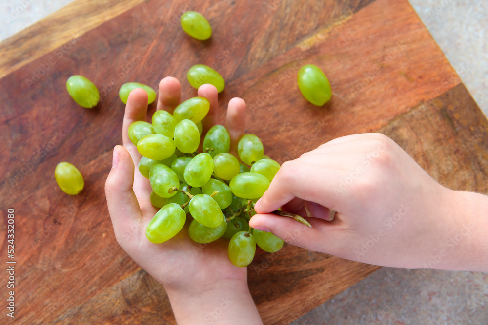 a woman's hand with green grapes, wooden background, concept of fresh sweet fruits and healthy food a woman's hand with green grapes, wooden background, concept of fresh sweet fruits and healthy food