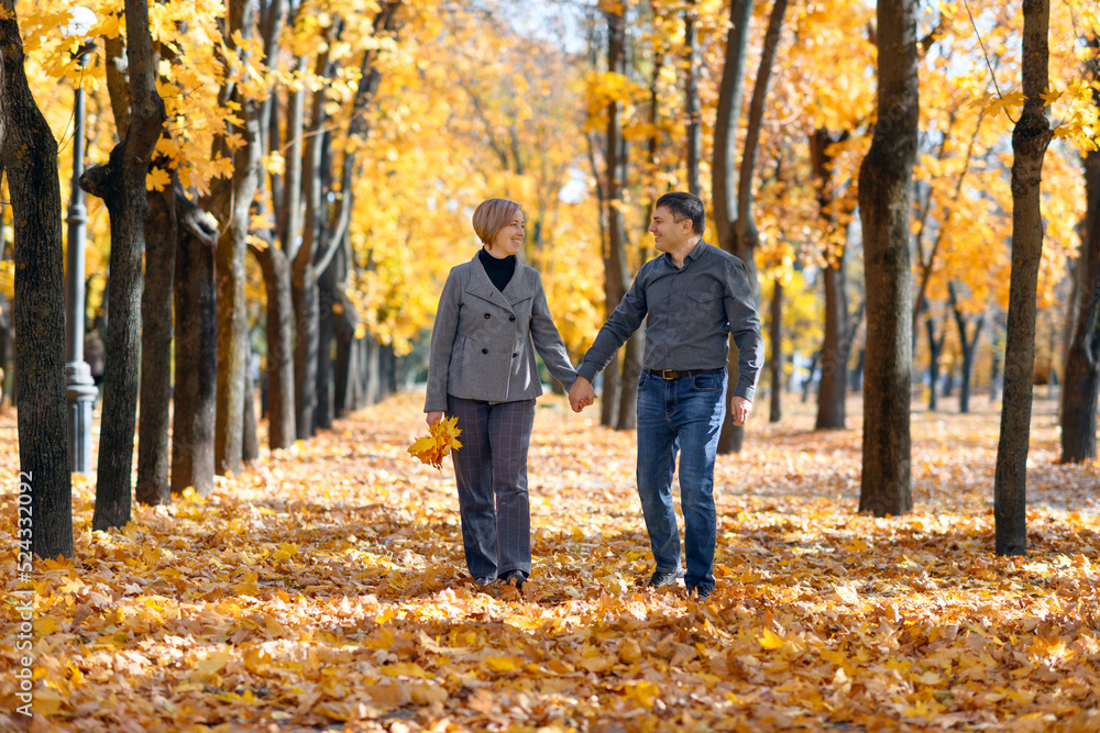 portrait of a romantic couple in an autumn city park, a man and a woman walking and posing against the background of yellow maple leaves, a bright sunny day