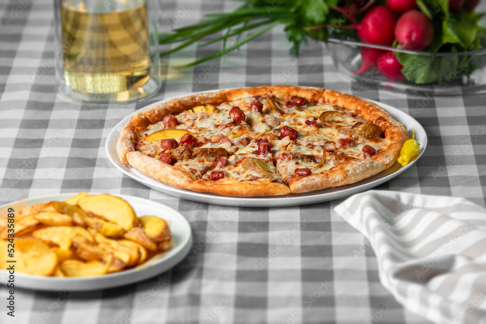 Bavarian pizza (mozzarella cheese, alpine sausages, baked potato wedges, bacon, sweet peppers, barbecue sauce) on a white plate on the table. Bavarian pizza (mozzarella cheese, alpine sausages, baked potato wedges, bacon, sweet peppers, barbecue sauce) on a white plate on the table.