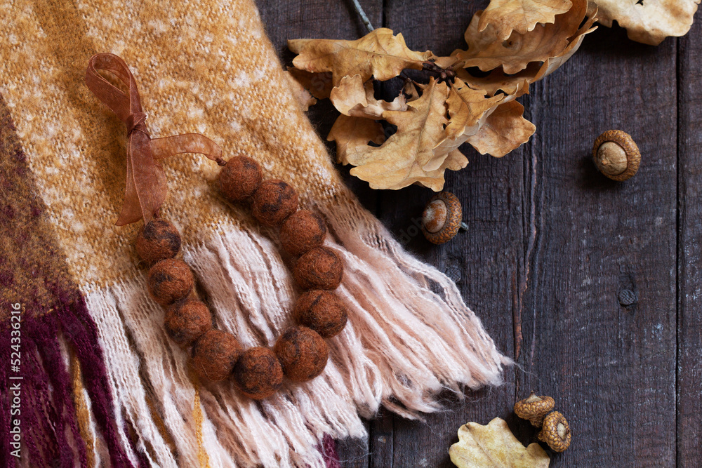 Woolen scarf, beads, dry oak branch and acorns on a wooden background.