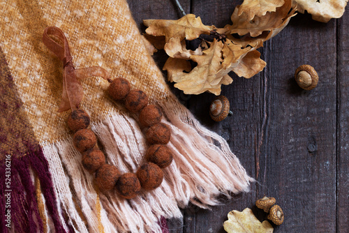 Woolen scarf, beads, dry oak branch and acorns on a wooden background. photo