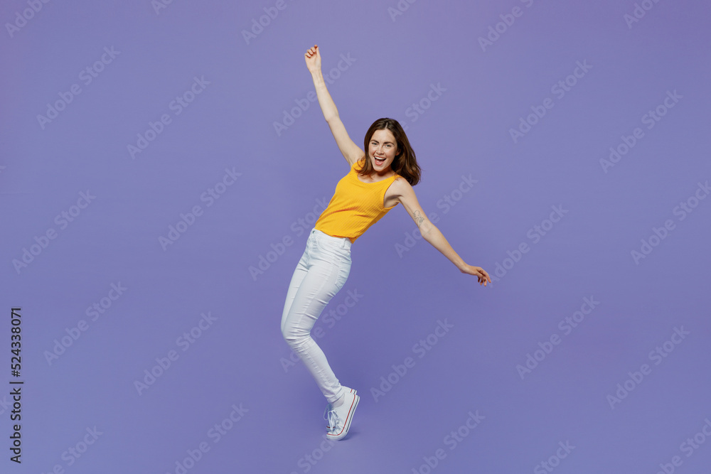 Full body young woman 20s she in yellow tank shirt stand on toes with outstretched hands leaning back dance isolated on plain pastel light purple background studio portrait. People lifestyle concept Full body young woman 20s she in yellow tank shirt stand on toes with outstretched hands leaning back dance isolated on plain pastel light purple background studio portrait. People lifestyle concept