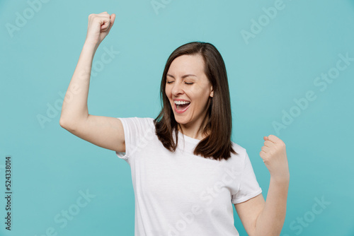 Young overjoyed woman 20s she wear white t-shirt doing winner gesture celebrate clenching fists say yes isolated on plain pastel light blue cyan background studio portrait. People lifestyle concept.