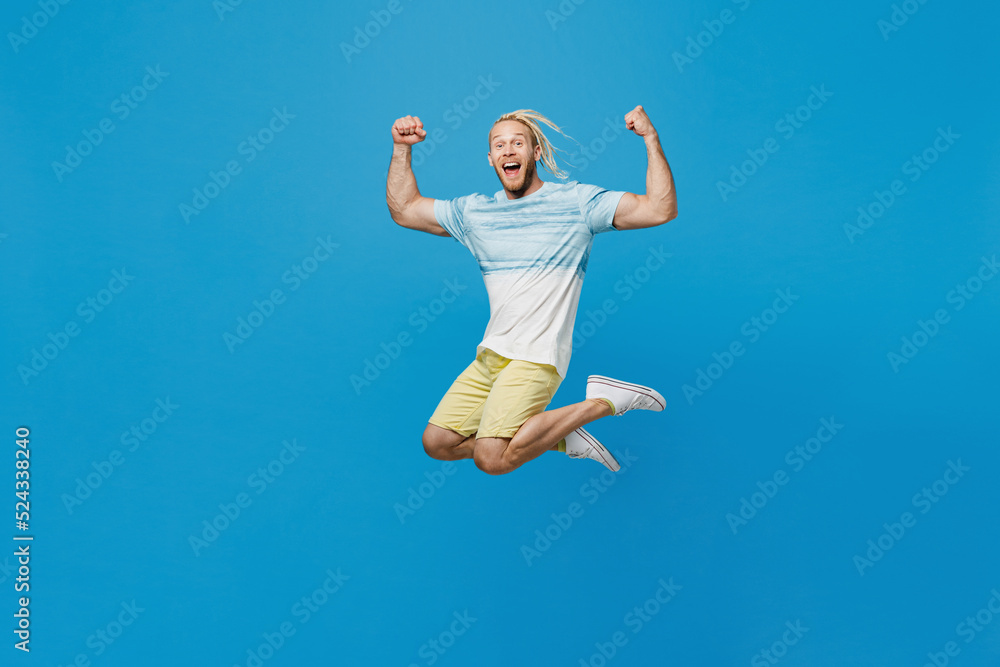 Full body young blond man with dreadlocks 20s he wear white t-shirt look camera jump high do winner gesture isolated on plain pastel light blue background studio portrait. People lifestyle concept. Full body young blond man with dreadlocks 20s he wear white t-shirt look camera jump high do winner gesture isolated on plain pastel light blue background studio portrait. People lifestyle concept.
