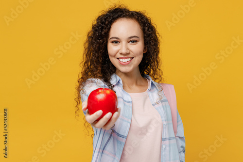 Young smiling happy cheerful cool black teen girl student she wearing casual clothes backpack bag hold giving apple isolated on plain yellow color background. High school university college concept.