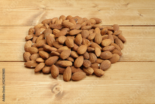 A heap of raw almonds on brown toned wooden table.