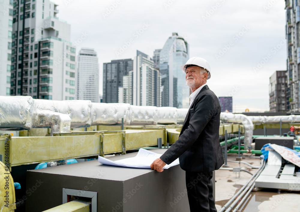 Senior engineer man stand in front of line of air vents and also using building drawing to finish his work in construction site. Senior engineer man stand in front of line of air vents and also using building drawing to finish his work in construction site.