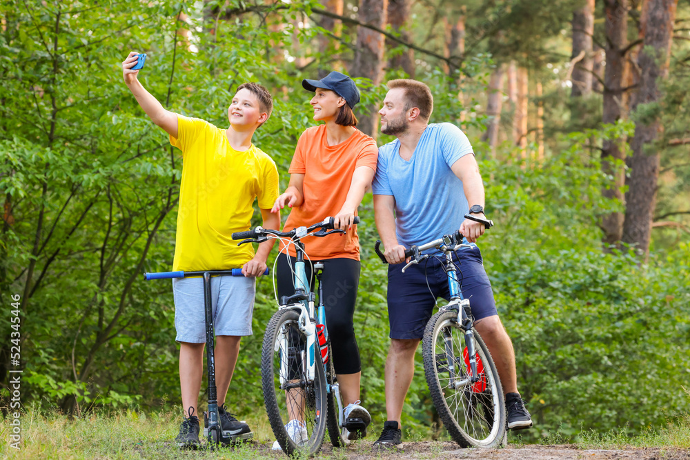 happy family takes a selfie while walking through the forest on bicycles. sports family in the forest ride bikes and take a joyful selfie. mom daddy son smile while taking a selfie