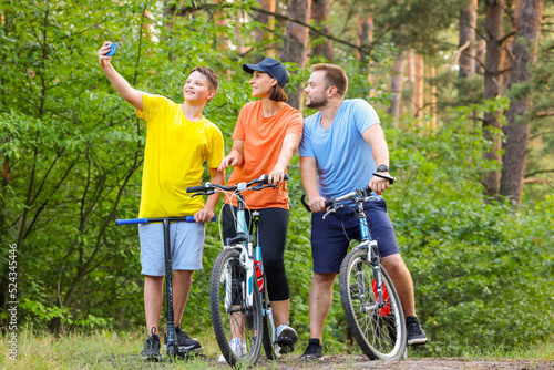 happy family takes a selfie while walking through the forest on bicycles. sports family in the forest ride bikes and take a joyful selfie. mom daddy son smile while taking a selfie