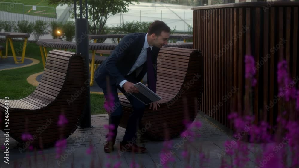 young businessman sits on bench in park during lunch break, holding tablet on which works. man in dark blue suit sits in chair and surfs Internet on computer. trader works everywhere. young businessman sits on bench in park during lunch break, holding tablet on which works. man in dark blue suit sits in chair and surfs Internet on computer. trader works everywhere.