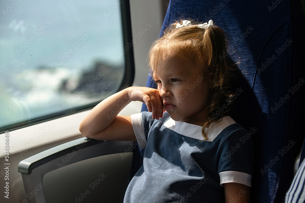 a little girl sits near the window in the train, family travel by rail