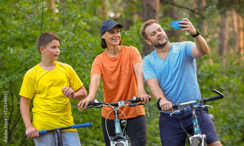 happy family takes a selfie while walking through the forest on bicycles. sports family in the forest ride bikes and take a joyful selfie. mom daddy son smile while taking a selfie © serhii