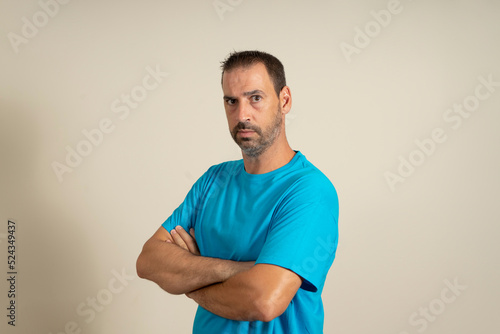 Portrait of a bearded spanish man posing with his arms crossed while looking at the camera very serious, isolated over beige background.