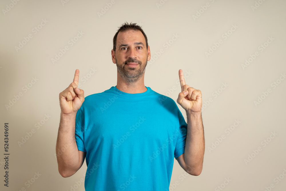 Latin attractive bearded man wearing blue t-shirt pointing up with finger isolated on beige background Latin attractive bearded man wearing blue t-shirt pointing up with finger isolated on beige background