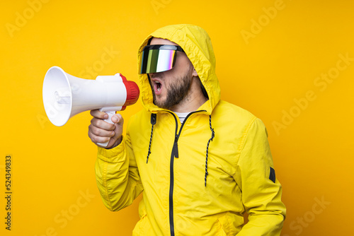 Young man in cyberpunk glasses shouting into a megaphone on a yellow background