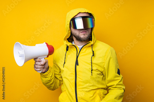 Young man in cyberpunk glasses holding a megaphone on a yellow background