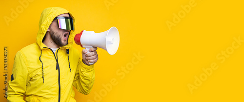 Young man in cyberpunk glasses shouting into a megaphone on a yellow background. Banner