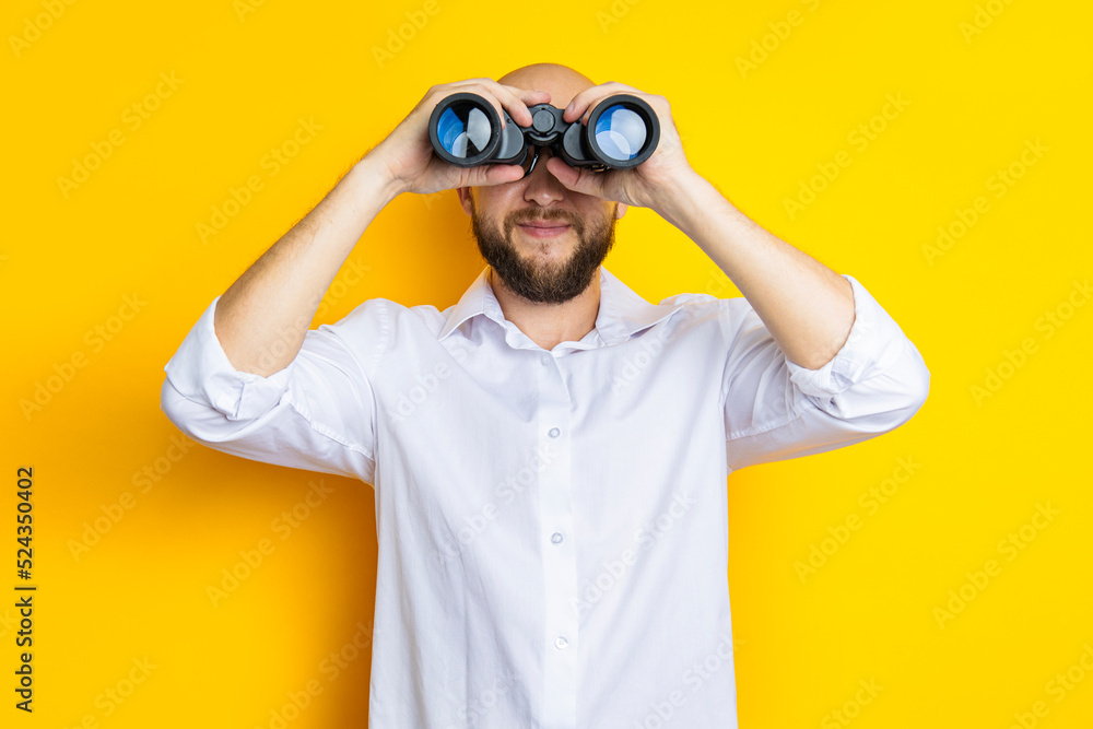 Smiling young man with beard looking through binoculars on yellow background Smiling young man with beard looking through binoculars on yellow background