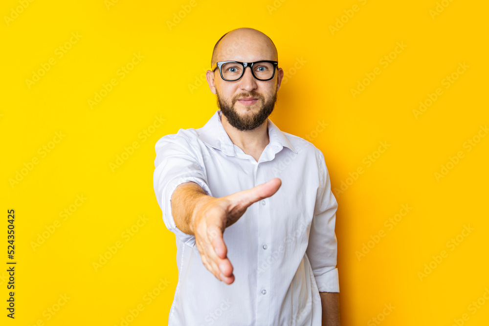 Young male extending his hand for a handshake greeting on a yellow studio background Young male extending his hand for a handshake greeting on a yellow studio background