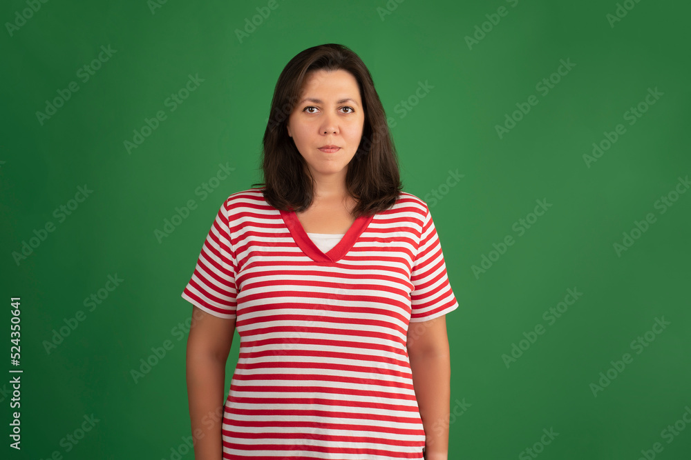 portrait of a confident woman looking at the camera wearing a red and white striped t-shirt standing against a green background with copy space portrait of a confident woman looking at the camera wearing a red and white striped t-shirt standing against a green background with copy space