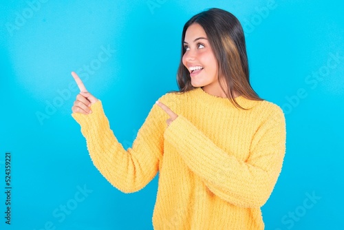 beautiful brunette woman wearing yellow sweater over blue background smile excited directing fingers look empty space