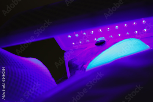 Express facial treatment with led therapy. Beautiful girl on a light therapy procedure. LED lamp with blue light. Safe skin care. Woman in protective glasses. Beauty and wellness concept. 