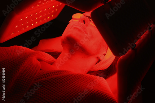 Express facial treatment with led therapy. Beautiful girl on a light therapy procedure. LED lamp with red and yellow light. Safe skin care. Woman in protective glasses. Beauty and wellness concept.