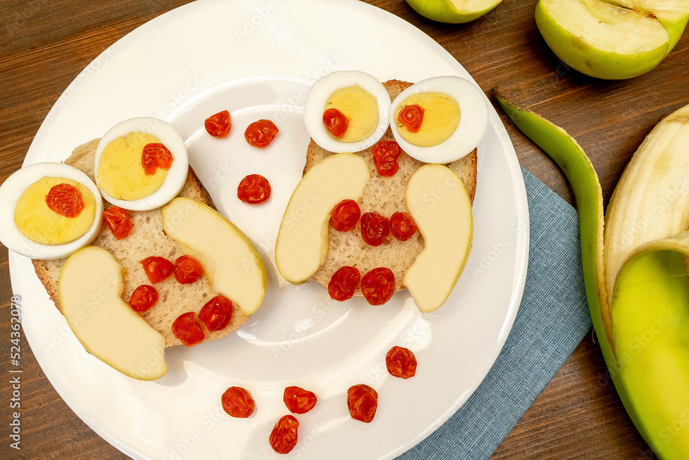 Funny owl face sandwich toast bread with chicken eggs, apple, banana, dried berry fruits on plate. Cute kids childrens baby's sweet dessert breakfast,lunch, food art on wooden background,top view Funny owl face sandwich toast bread with chicken eggs, apple, banana, dried berry fruits on plate. Cute kids childrens baby's sweet dessert breakfast,lunch, food art on wooden background,top view