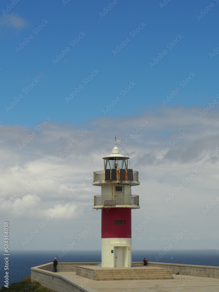 A lighthouse in the cliff with the clouds and the ocean in the background.