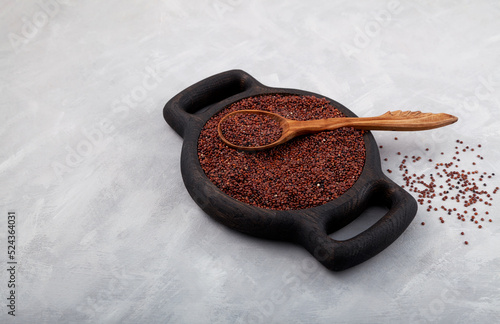 Red quinoa grain in wooden plate and wooden spoon on grey background. Selective focus, copy space photo