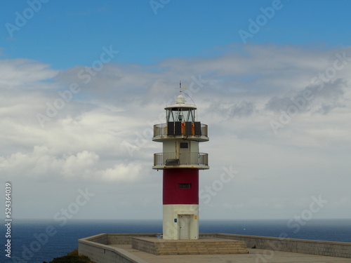 A lighthouse in the cliff with the clouds and the ocean in the background.