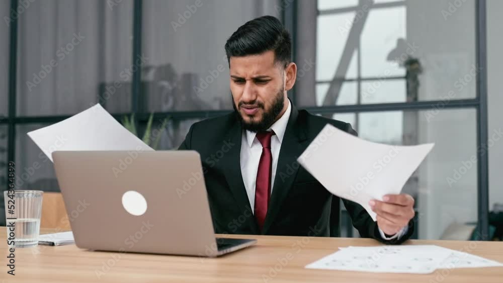 Disappointment stressed indian or arabian business man, sit at work desk with laptop in modern office, works with documents, upset with financial report, analyzes the result of work, feels frustrated Disappointment stressed indian or arabian business man, sit at work desk with laptop in modern office, works with documents, upset with financial report, analyzes the result of work, feels frustrated