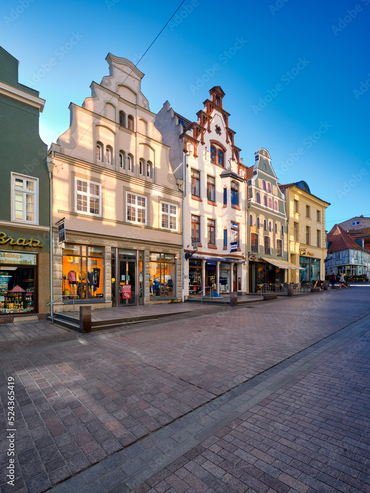 Old historic buildings, houses in Wismar, Germany. Empty square early morning. Sunny day with blue sky, sun flare.