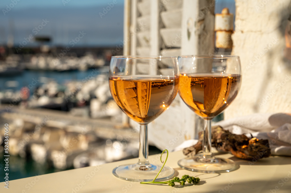 Summer party with cold rose wine in glass served on outdoor terrace in sunlights with view on old fisherman's harbour with colourful boats in Cassis, Provence, France